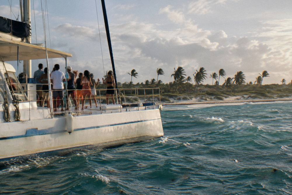 Group of adults dancing on a catamaran deck in late afternoon light