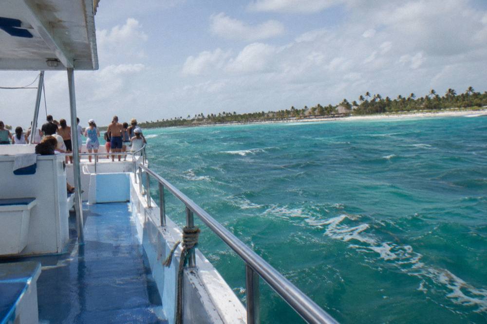 A group of adult passengers on a boat deck with drinks in hand under a sunny sky